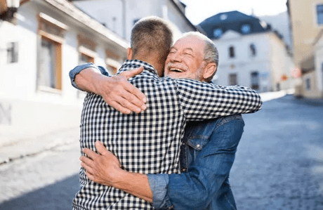 Older man hugging younger man in street.